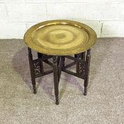 A brass decorative tray topped table, circa 1900, with embossed decoration and fret carved folding
