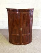 A George III mahogany corner cabinet, circa 1790, with two bow front panelled doors, enclosing