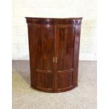 A George III mahogany corner cabinet, circa 1790, with two bow front panelled doors, enclosing