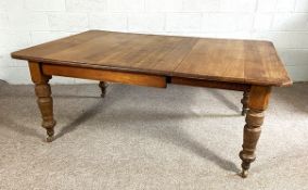 A late Victorian oak extending dining table, wind out, with additional leaf and set on turned legs