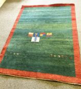 A late 20th century decorative rug, with figures on a green field, with red border, possibly