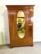 An Edwardian mahogany inlaid wardrobe, with oval mirrored door and single long drawer (Associated