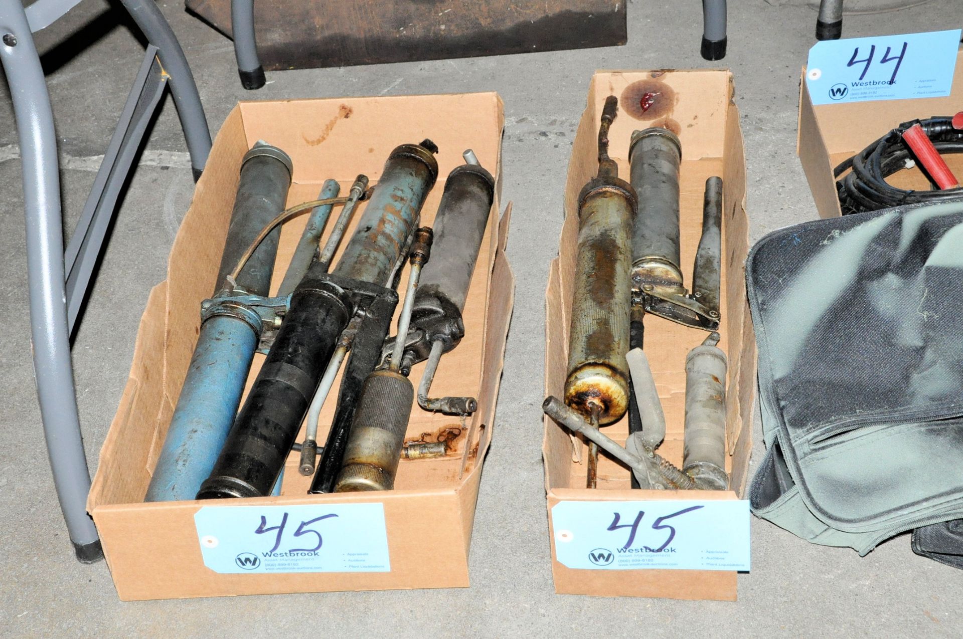 Lot-Various Grease Guns in (2) Boxes on Floor Under (1) Table