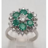 A Very Pretty 18K White Gold, Emerald and Diamond Ring. Floral design with a central diamond, six