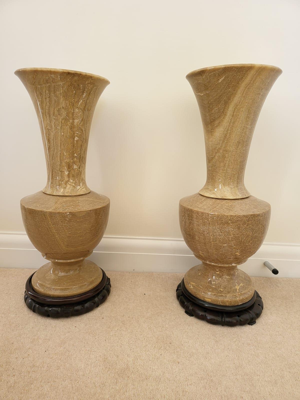 A Pair of Large Beige Polished Stone Vases. Both on dark wooden stands. 56cm tall. 20cm width.