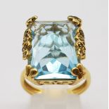 An 18K Yellow Gold Blue Topaz Ring. Pale blue 10ct stone in a scroll setting. 8.81g total weight.