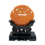 An antique, Chinese, hand carved orange jade amulet on a custom made wooden carved base. The
