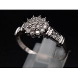 A 9K white gold ring with a cluster of diamonds and further diamonds on shoulders (diamonds 0.30