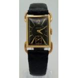 A 14 K yellow gold Le Coultre watch. 27 x 20 mm case, gold bezel, black face with gold hour marks