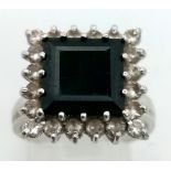 An 18K White Gold Emerald and Diamond Ring. Square-cut dark green emerald with a white diamond