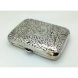 An Antique Sterling Silver Cigarette Case. Decorative scroll engraving. Gilded interior. 9 x 6cm.