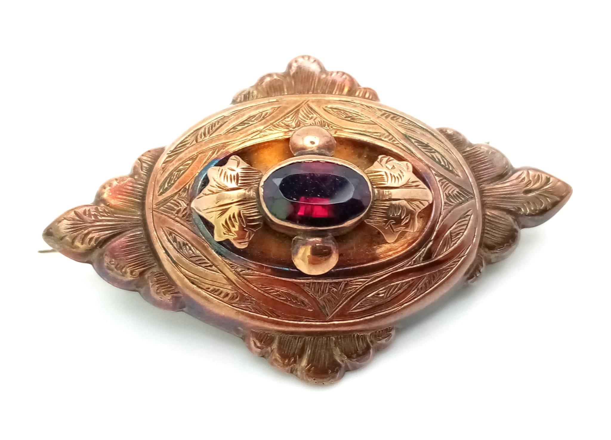 An Antique Victorian Mid Karat Rose Gold Mourning Brooch. Central oval garnet with memento capsule