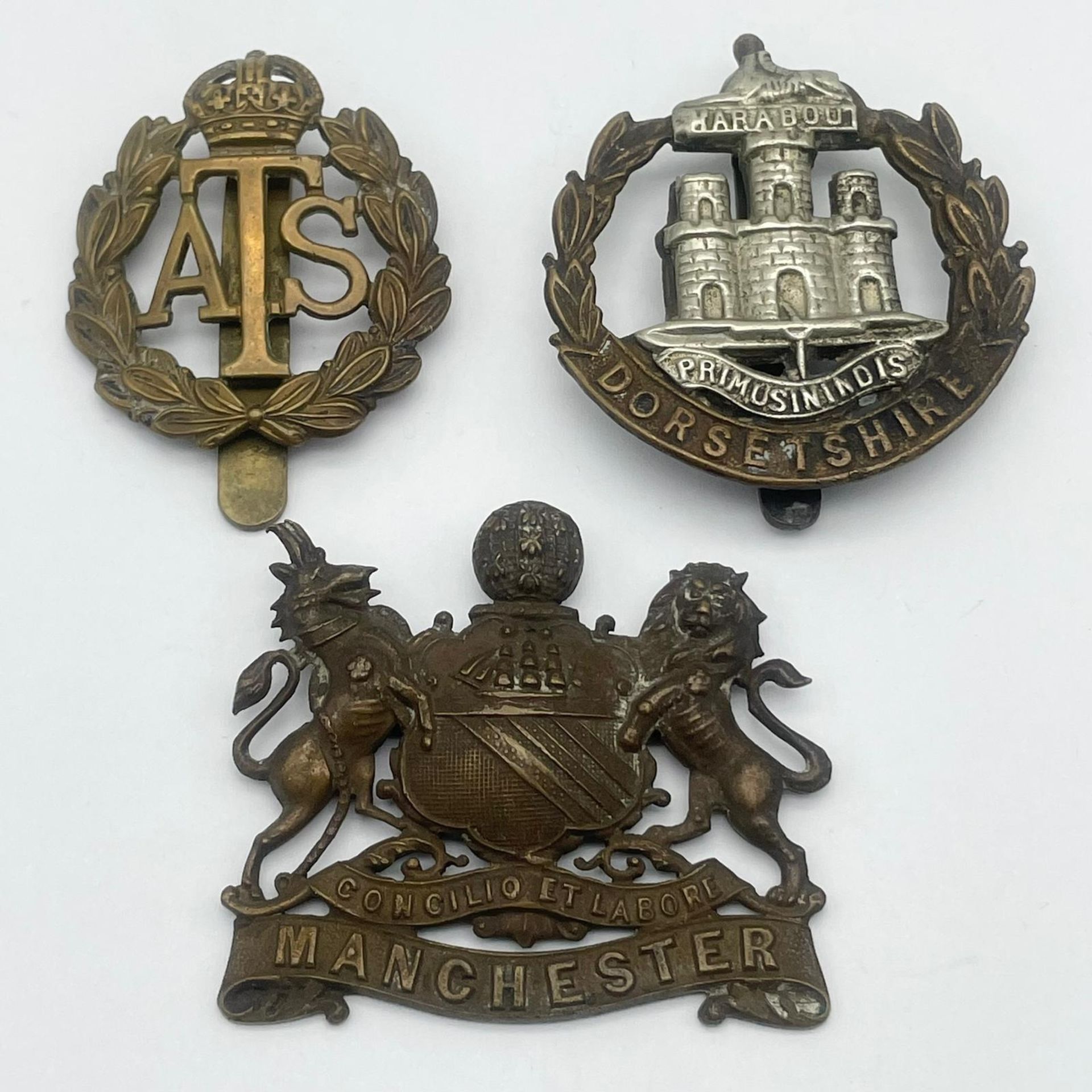 Three British Military Cap Badges: WW1 Dorsetshire Regiment Corp, WW2 Royal Artillery Manchester and