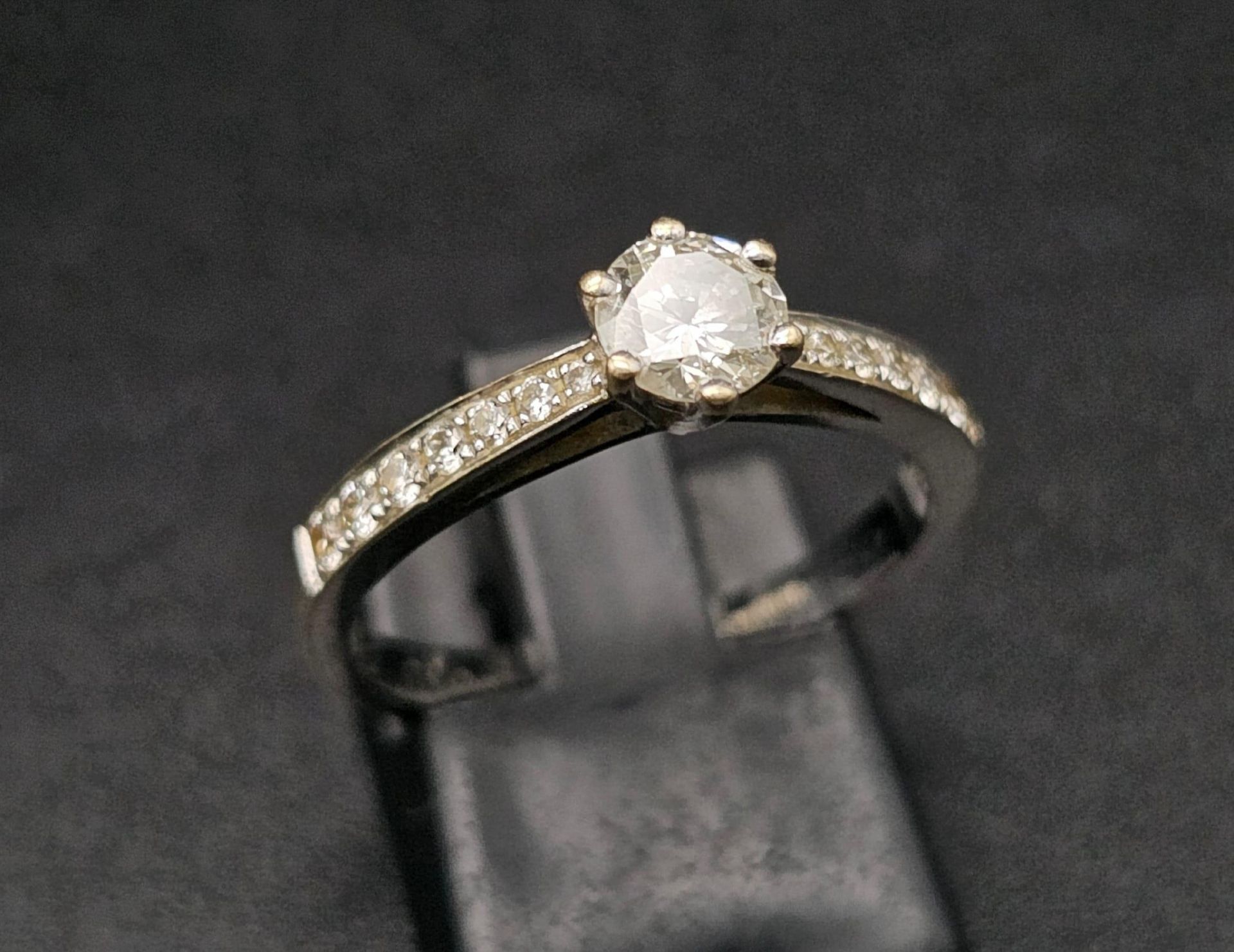 An 18 K white gold ring with a brilliant cut diamond and more diamonds on the shoulders of the ring.