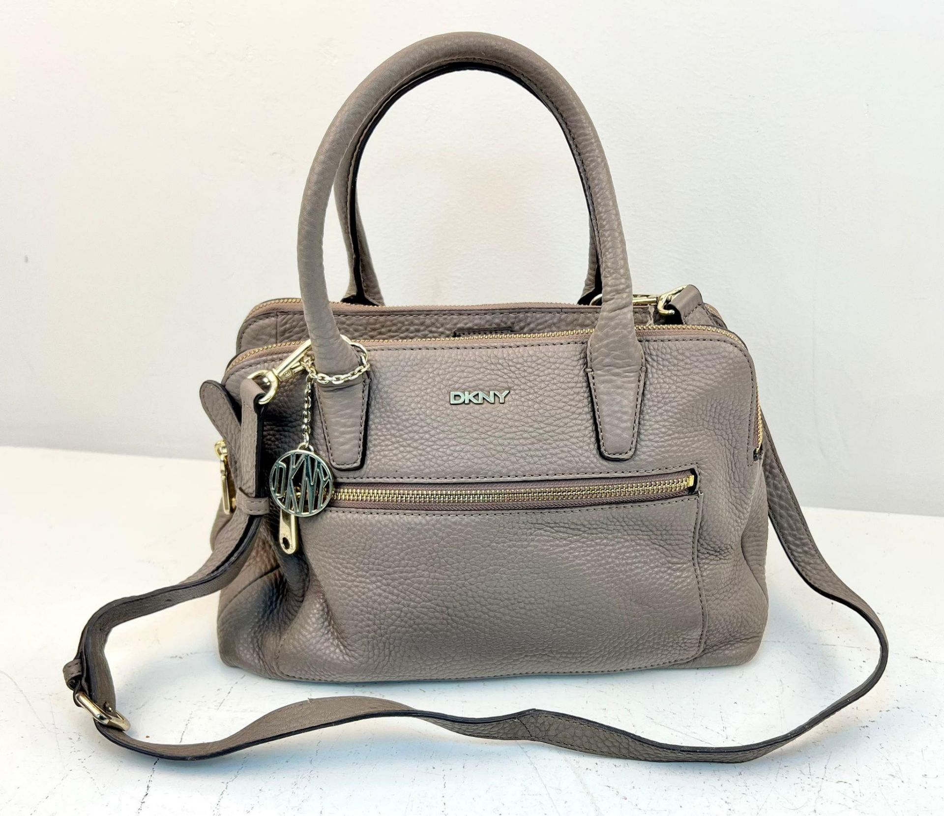 A DKNY Brown Leather Handbag with Shoulder Strap. Gold-tone hardware. Exterior zipped compartment.