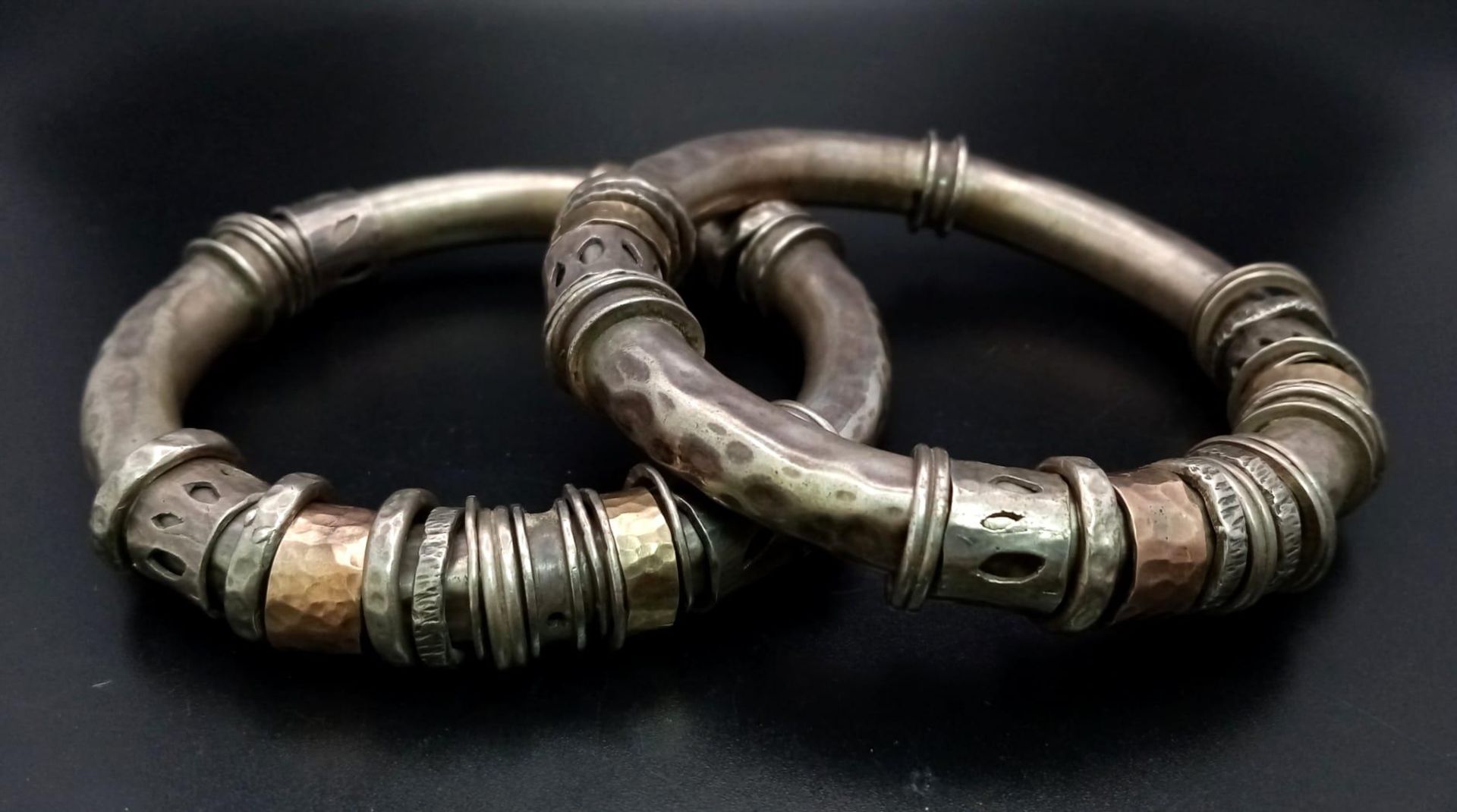 A pair of silver and gold bangles in tubular form with loose ring decoration. The bangles have a
