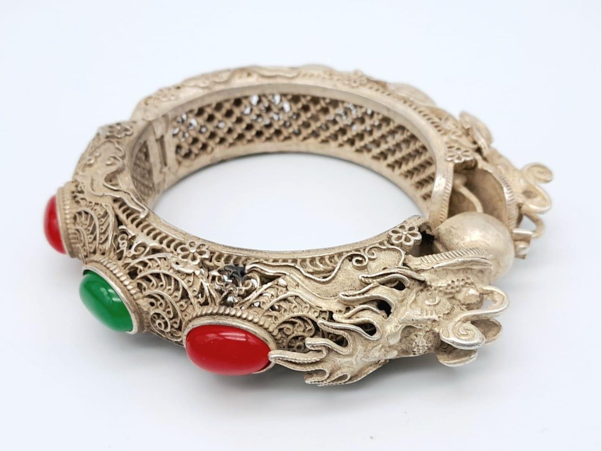 An antique, Chinese silver, filigree bangle, in the shape of two dragons with green and red jade