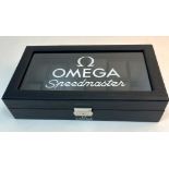 A Twelve Watch Omega Display Case. Carbon fibre effect finish. Black felt on base. 52mm spaces.