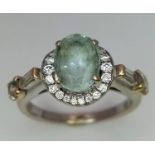 A 14 K white gold ring with an oval cut aquamarine surrounded by a halo of round cut diamonds and