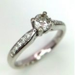 A PLATINUM DIAMOND SOLITAIRE RING WITH A ROUND BRILIANT CENTRE STONE AND DIAMOND SET SHOULDERS,