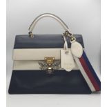 A GUCCI Large QUEEN MARGARET TOP HANDLE BAG in Black with a beige strip across the front. The bag