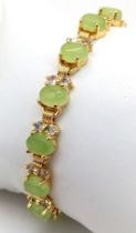 A Green Jade Tennis Bracelet. Oval jade pieces set in gilded metal with white stone decoration.