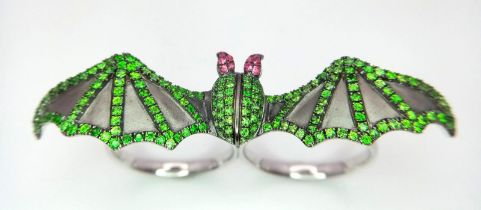 An 18K White Gold Bat Ring! An Emerald and Ruby bat flies over two gold expandable rings. Size P -