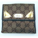 A Gucci Monogram Wallet. Canvas exterior with brown leather trim and gold-tone details. Flap closure