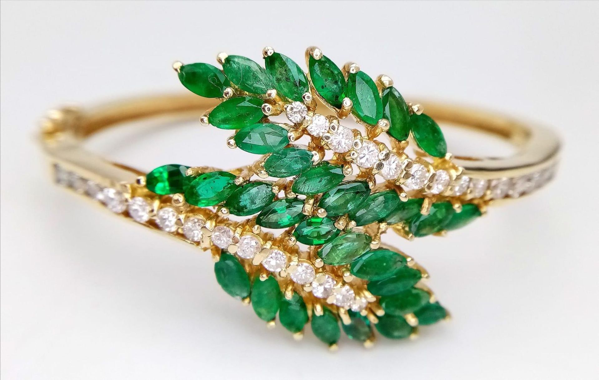 A DIAMOND AND EMERALD LEAF DESIGN BANGLE IN CROSSOVER STYLE SET IN18K GOLD . 33.5gms 10457
