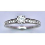 An 18K White Gold Diamond Ring. Central brilliant round cut diamond with diamonds on shoulders. 0.