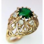 A Vintage 9K Yellow Gold Emerald and White Stone Ring. Round cut emerald with a white stone halo