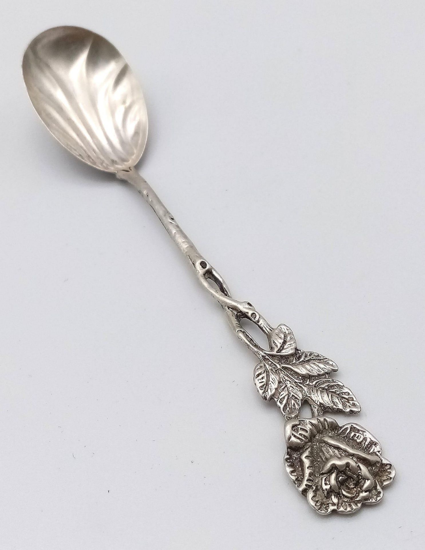 An antique silver spoon. A rose designed handle which flows down to a clam-shell like spoon bowl.