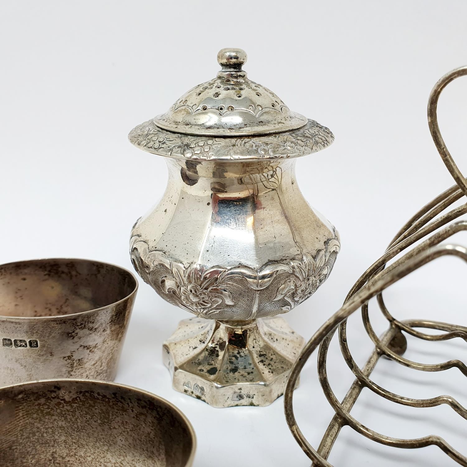 A Indian silver coloured metal pepperette, a four division toast rack, and a set of napkin rings,