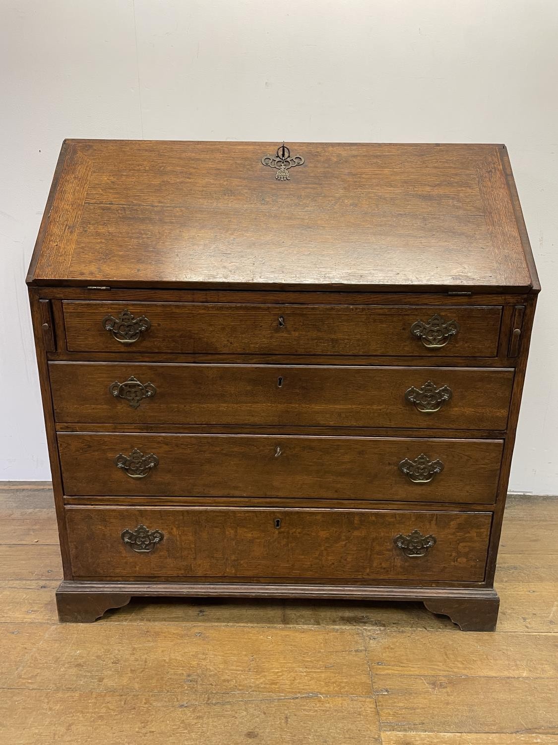 A George III oak bureau, the fall front to reveal a fitted interior, above four graduated drawers,