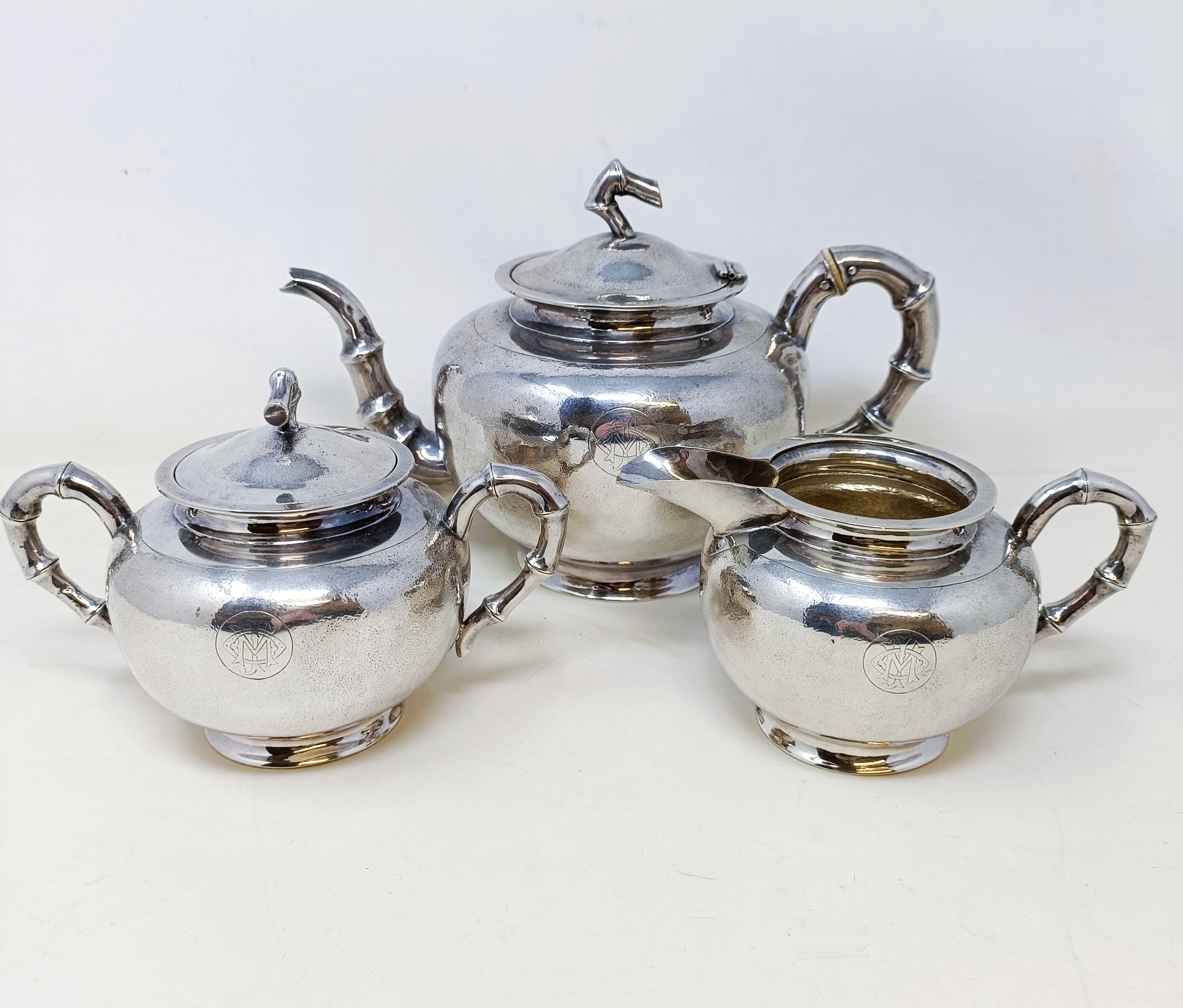 A Chinese silver coloured metal three piece tea set, monogrammed, with hammered style decoration and