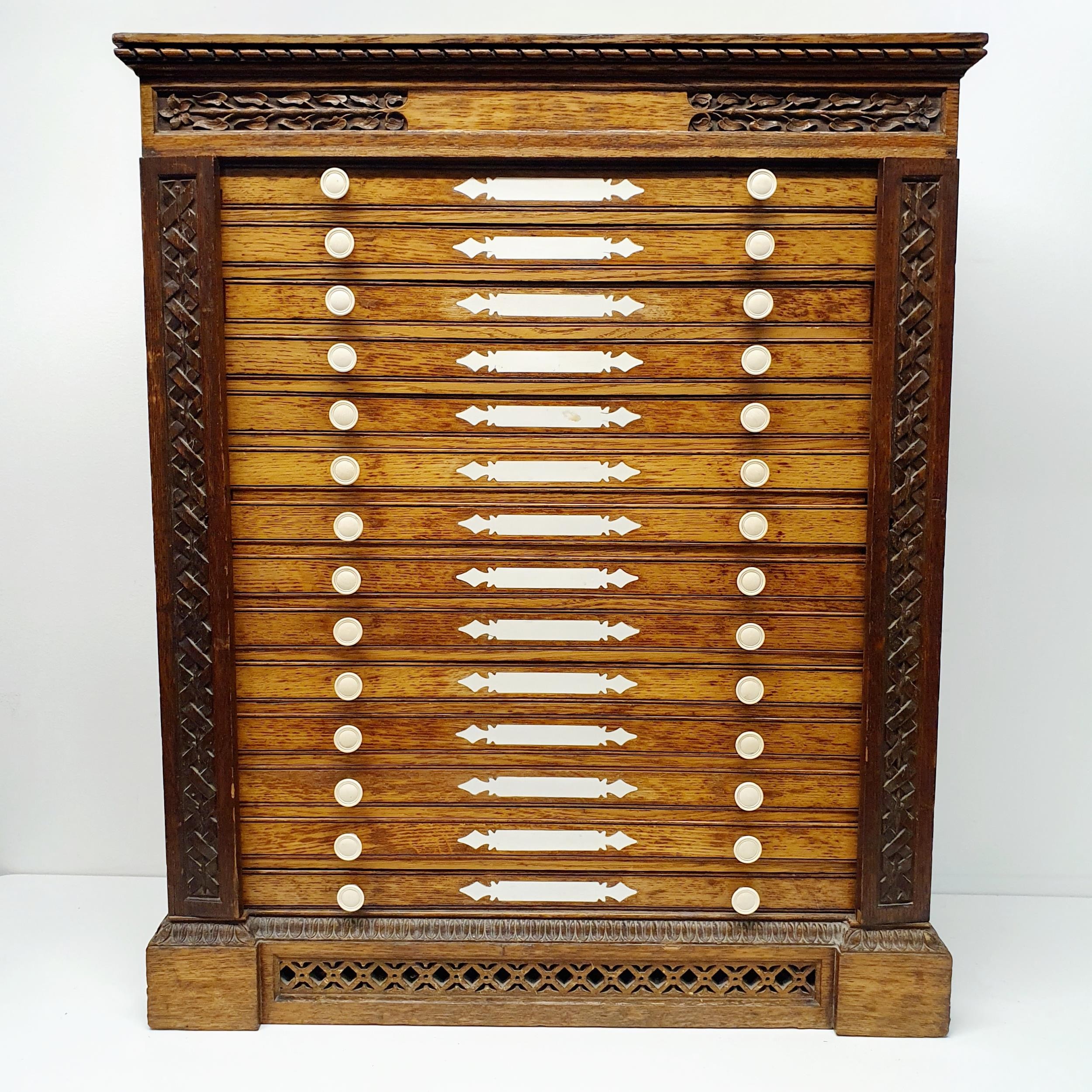 A late 19th century oak collectors chest, with a floral carved frieze, fourteen drawers, 70 cm x