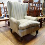 An upholstered wing armchair, on turned front legs