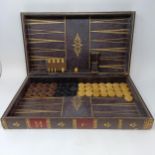A backgammon board in the form of a book, with carved wooden draughts and dice, 47 cm wide Very worn