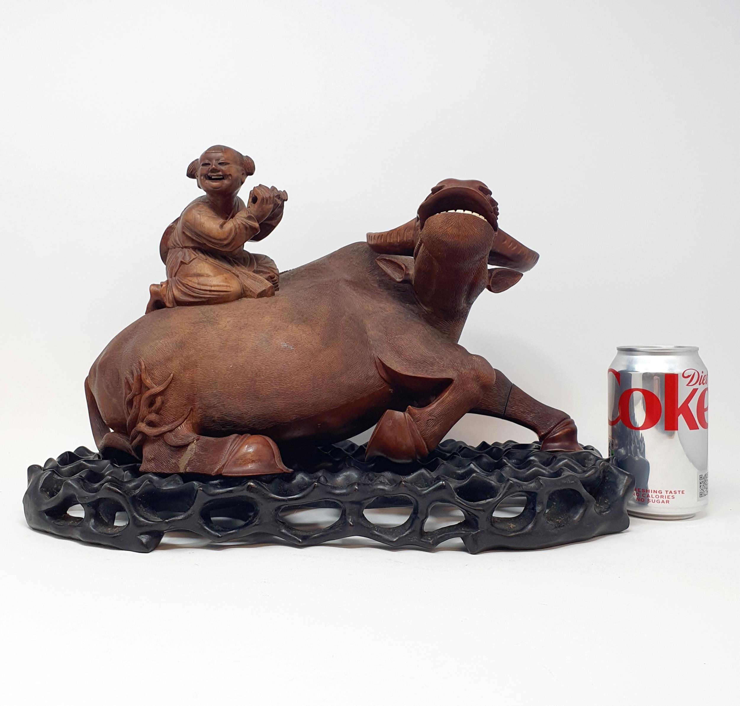 A Chinese carving of a water buffalo, with a seated figure, on a hardwood stand, 40 cm high