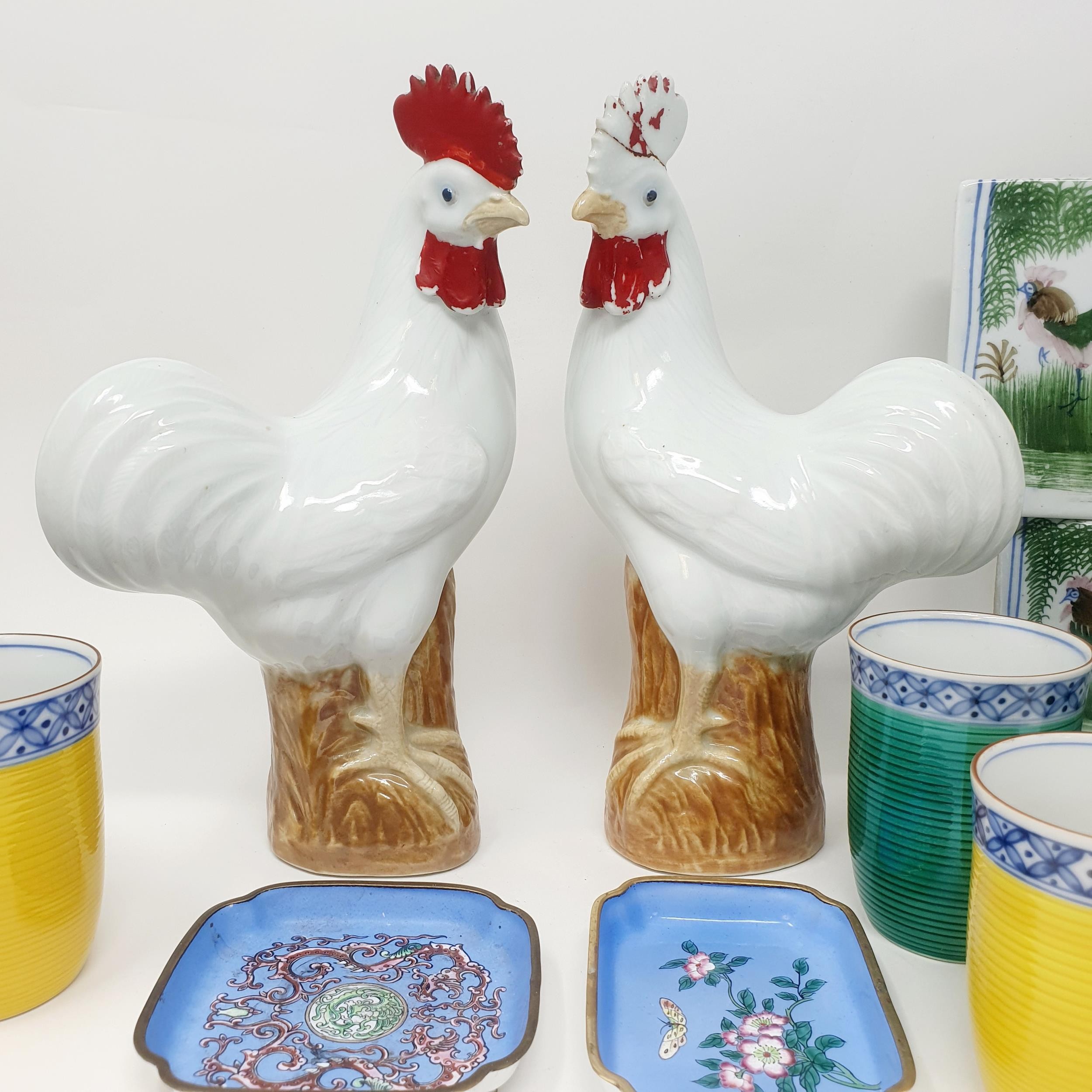 A pair of Chinese cockerels, 25 cm high, two cushions, four beakers and two enamel dishes (10)