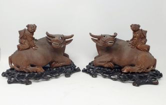 A pair of Chinese carvings of oxen, with figures on their backs, on pierced stands, 25 cm wide (2)