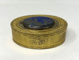 A gilt metal oval box, the top inset with a blue hardstone plaque, 8 cm wide