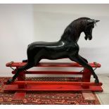 A large black vintage fiberglass Haddon Rockers rocking horse on a red wooden base, missing tack