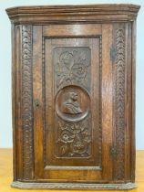 An 18th century oak corner cupboard with carved design of gentleman with flowers and leaves