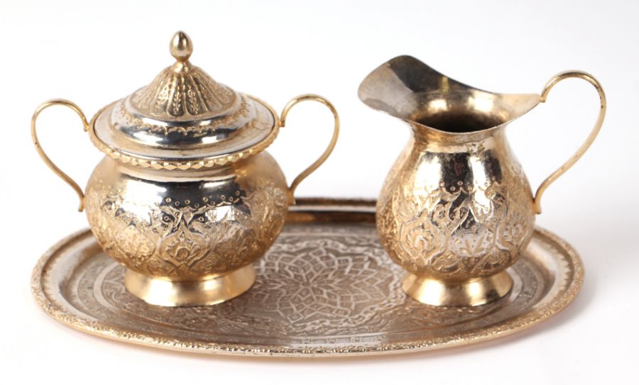 A Persian gilt metal oval tray, milk jug and sugar bowl with chased decoration, the tray 23cms