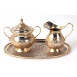 A Persian gilt metal oval tray, milk jug and sugar bowl with chased decoration, the tray 23cms