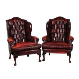 A pair of Georgian style button backed leather wingback armchairs.