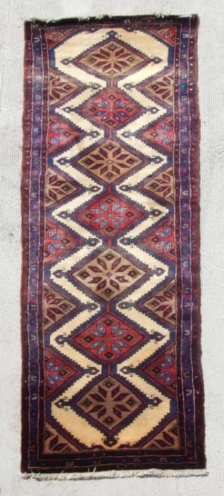 A Persian hand knotted woollen runner with stylised diamond motifs on a beige ground, 265 by