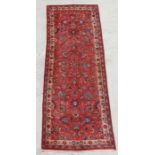 A Persian hand knotted runner with central floral design within floral borders, on a red ground, 295