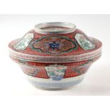 A large Japanese rice bowl and cover decorated with vignettes of flowers, on a red ground, 26cms